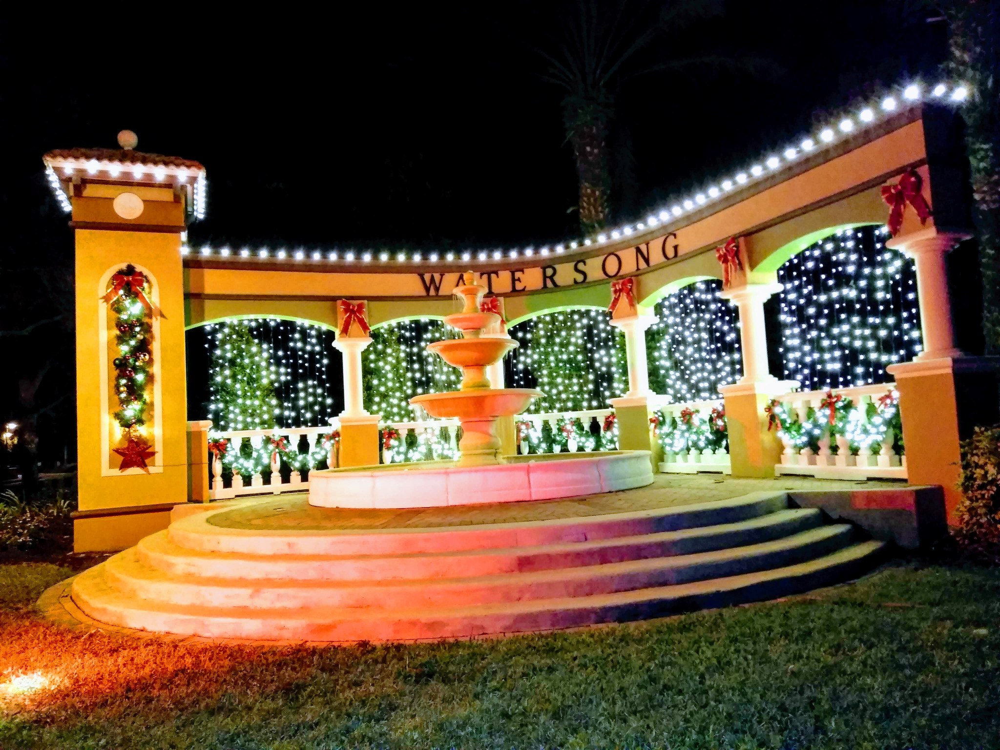 Watersong community entrance illuminated with white holiday lights and red bows